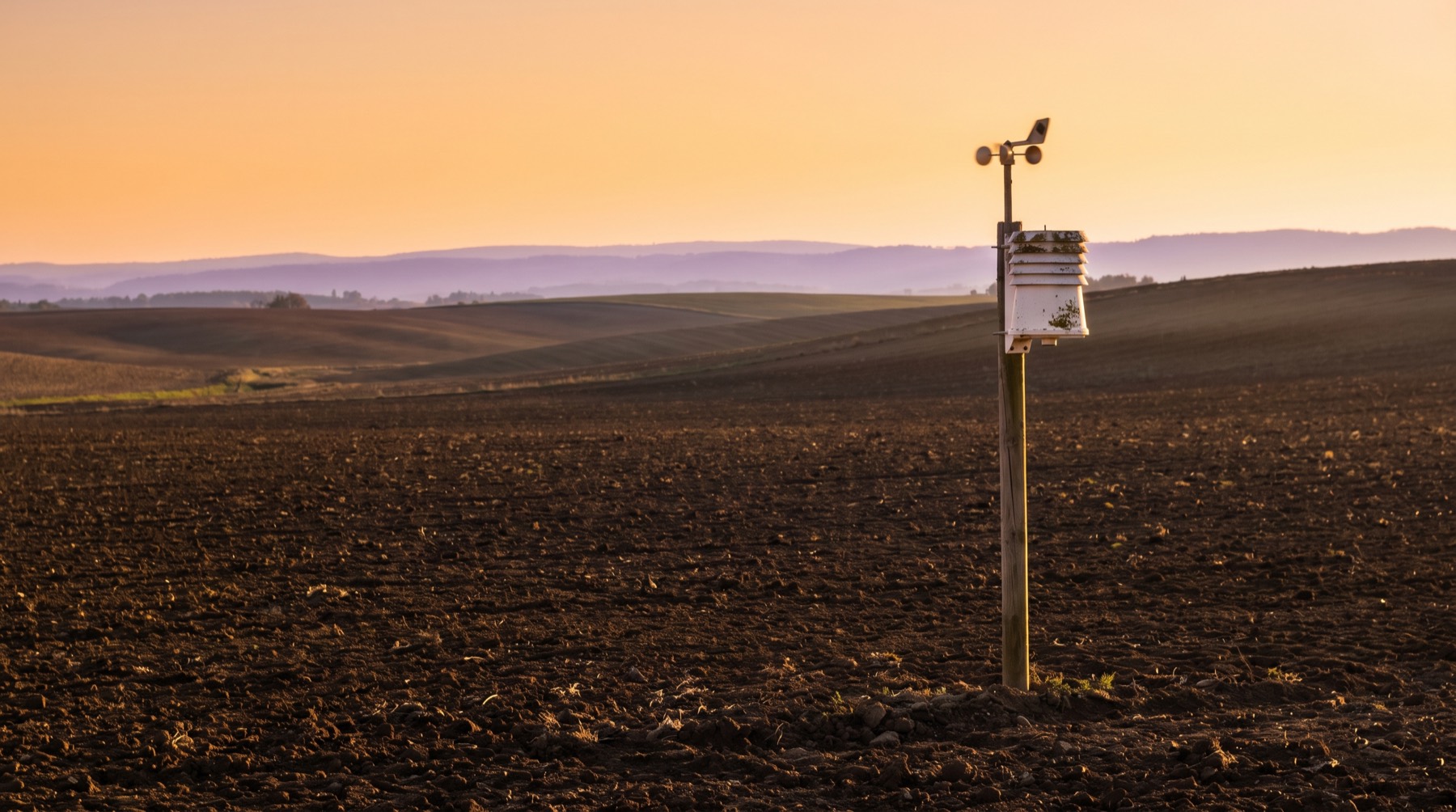 Un champ labouré au coucher du soleil dans le sud de la France, une petite station météo sur un poteau au premier plan